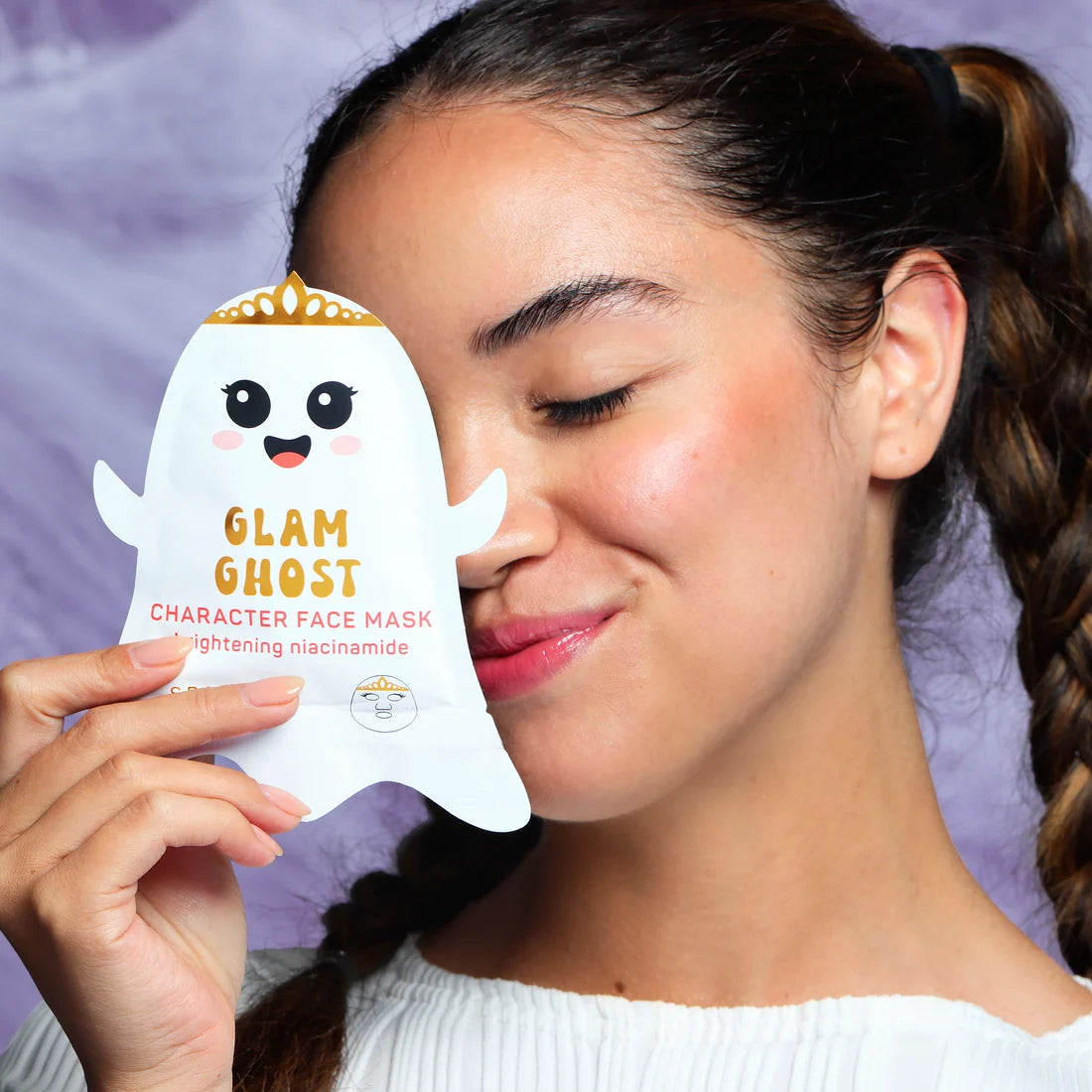 Glam Ghost character face mask sheet held near woman’s cheek