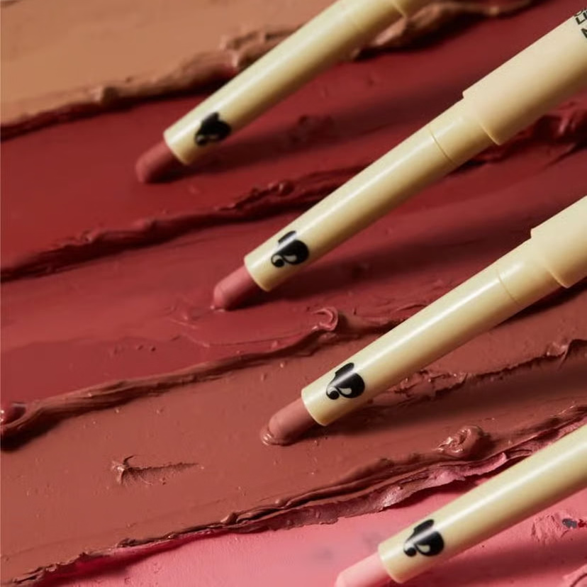 Close-up of multiple pale yellow lip pencils over dark rose-red swatches