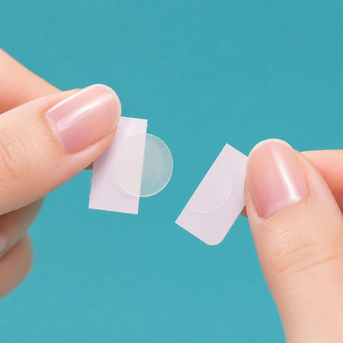 Thin clear acne patches being applied by fingertips, two pieces
